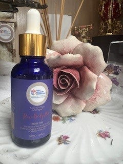 A bottle of Wellness Oil from Well Building Connection – Rose and Lavender on a clear surface with its packaging box in the background, featuring a blue and white color scheme.